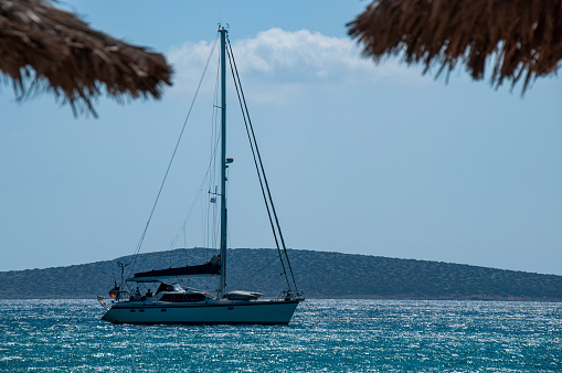 A sailboat drifts by beach umbrellas on the shores of Ios, Greece