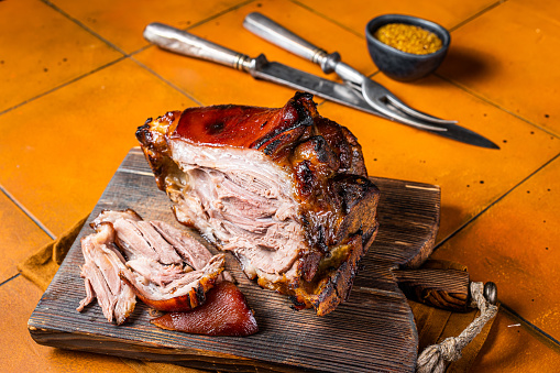 Roasted pork Shank, knuckle on a wooden board. Orange background. Top view.