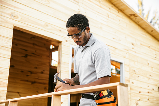 Construction worker nailing porch railing of small wooden house