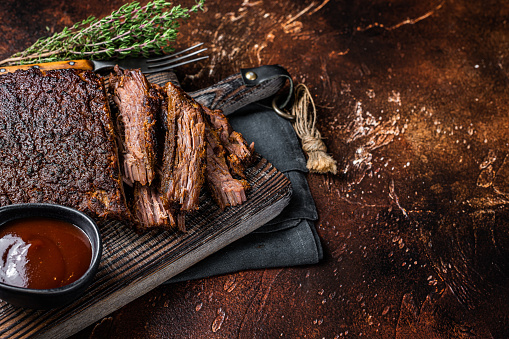 Traditional smoked barbecue wagyu beef brisket on wooden board. Dark background. Top view. Copy space.