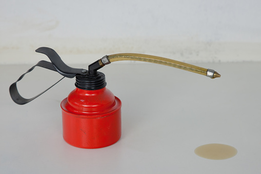 A red oil can with a flexible spout stands on the white workbench. From his tip Oil dripped onto the work surface.
