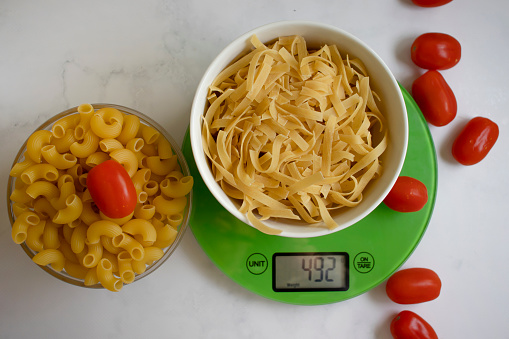 Kitchen scales, dry pasta, tomato on a light background