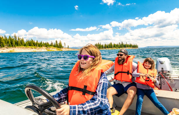 행복 한 어린 소녀는 가족과 함께 경치 좋은 호수에서 작은 모터 보트를 조종하는 구명 조끼를 입고, 자연 ��속에서 공생합니다. - boat safety 뉴스 사진 이미지