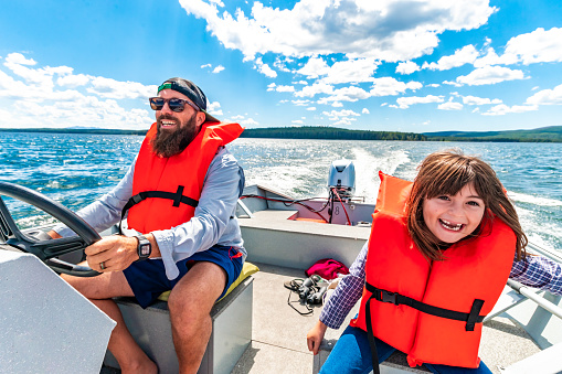 istock Happy father and daughter wearing life jackets on a small motor boat on a scenic lake with his family, togetherness in nature 1456266279