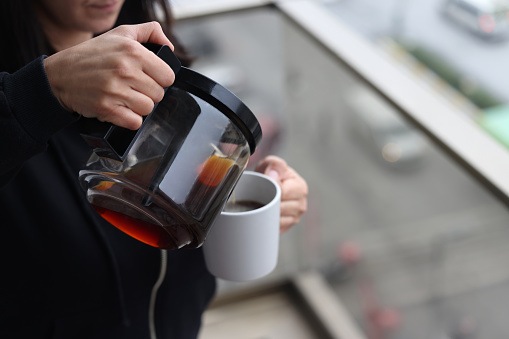 A woman pouring hot, freshly brewed coffee into her mug to begin her day with a surge of joy and energy.