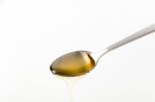 Metal spoon pouring fresh honey on white background