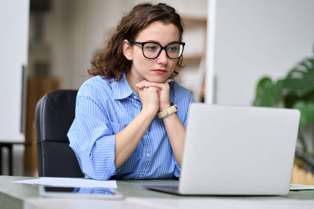 istock Young serious business woman using laptop watching online webinar at work. 1456275153