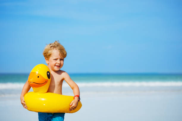 istock Blond boy with inflatable yellow duck buoy stand on sand beach 1456275806