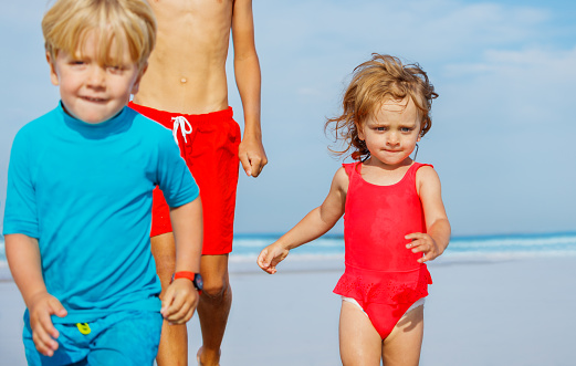 Close portrait of a group of three children boys and girl run on sand beach wear swimsuits during hot summer day