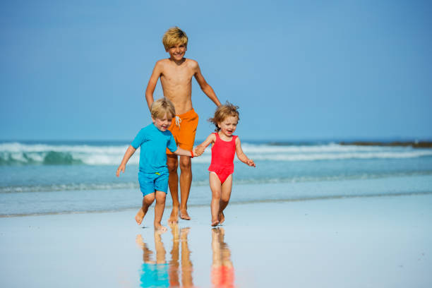 istock Group of three children run on sand beach holding hands 1456275817