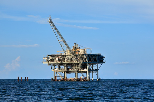 Oil rig offshore platform and support vessel. Blue clear sky, sea surface
