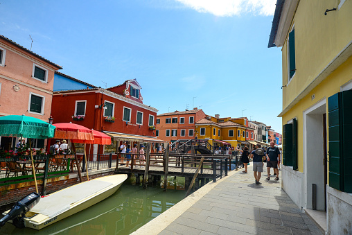 Burano Island, Venice, Italy - July 4, 2022:Tourists walking on the main street of Burano island, colorful houses on the canal, Famous travel destination. Venice, Italy.