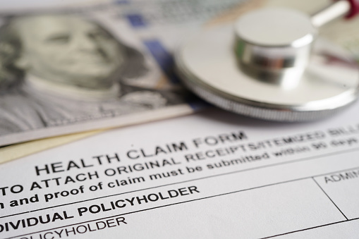 Health claim form with stethoscope and US dollar banknotes, insurance accident medical concept.