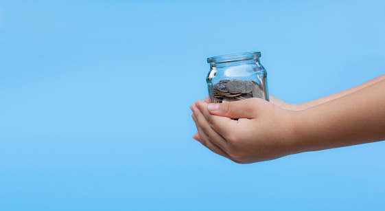 Child's hand holding a glass jar with money coin. Concept for education, save money, business, financial and funds. Background of success in the future.