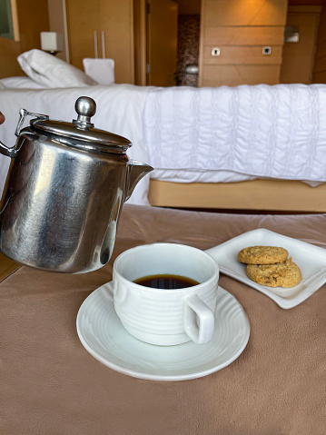 Stock photo showing close-up view of a cup of black coffee about to have  cold milk be poured into it from a stainless steel milk jug. The freshly brewed coffee is part of a room service breakfast, being served on a table.