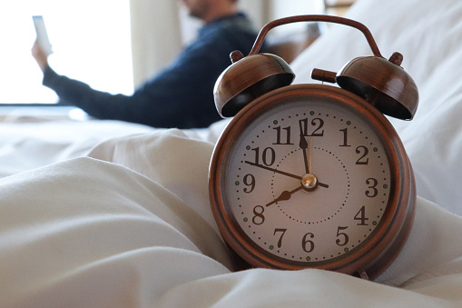 Stock photo showing close-up view of retro, double bell, analogue alarm clock sitting on duvet bedding.