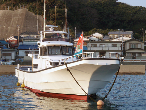 Typical white painted Japanese fishing boat moored at the cove port sea surface.