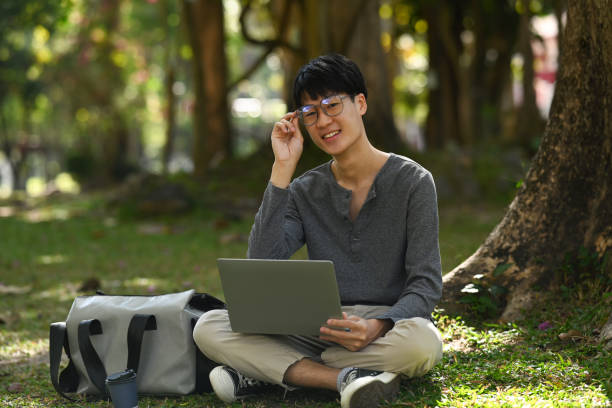 istock Pleasant asian man using laptop under a tree surrounded by beautiful nature. Education and lifestyle concept. 1456317966
