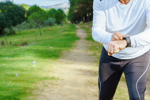 man training in the field with his smart watch wearing black pants and white t-shirt a pine forest in the background