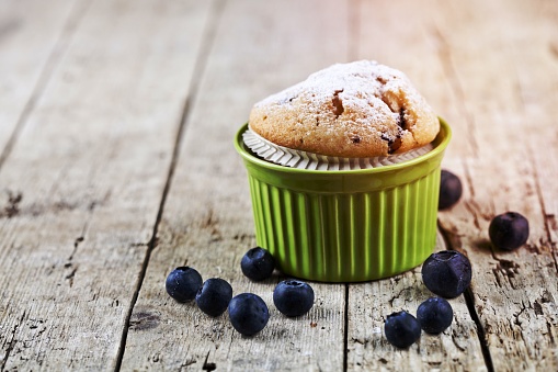 Homemade fresh muffin on ceramic green bowl with blueberries on rustic wooden table background.