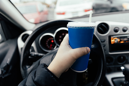 Human hand holding a drink cup while inside a parked car.