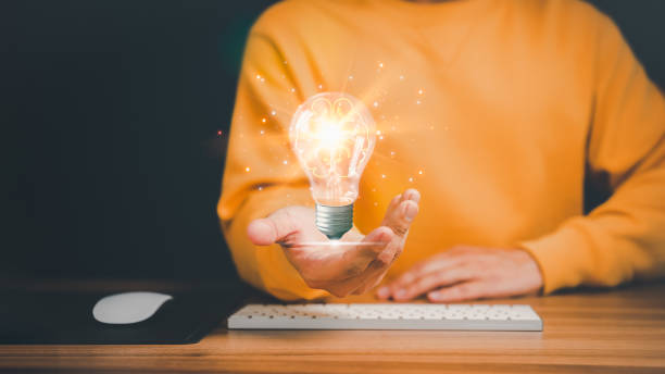 uomo che tiene una lampadina astratta incandescente con una tastiera del computer sul tavolo. idee di problem solving aziendale e idee di marketing creativo inventare e imparare cose nuove. - inspiration ideas light bulb computer mouse foto e immagini stock