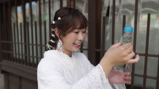 Woman in white lace kimono drinking a bottle of  ‘ramune’ soda in traditional Japanese town