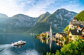 Panorama view of famous old town Hallstatt and alpine deep blue lake with tourist ship in scenic golden morning light