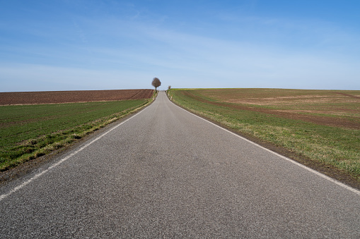Straight rural road between farmland in the countryside on a cold day with blue sunny sky in spring