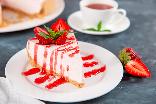 Sweet breakfast, tea and delicious cheesecake with fresh strawberries and mint, homemade recipe without baking, dark blue stone table. Copy space.
