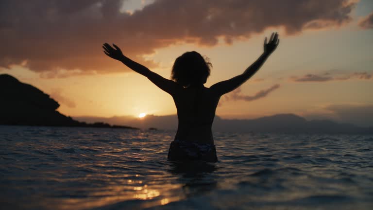 African ethnicity woman in the sea at sunset. Meditating and praying. One with nature