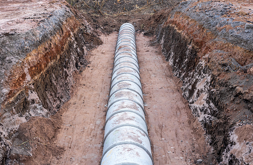 A view from above, a large circular concrete sewer mounted in the ground awaiting a landfill near the cross section beneath a rural road that has been renovated during the dry season.