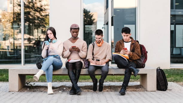 Diverse students using smartphones on bench stock photo
