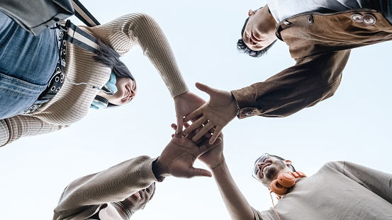Low angle view of a A group of mulitethnic group of students join hands to form a team