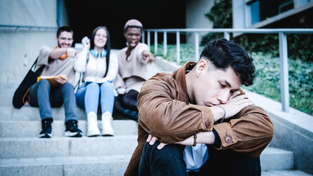 A group of students bulling an hispanic man sitting on the stairs outdoors stock photo