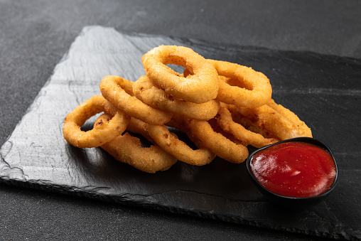 Calamari rings deep-fried in breading. Crispy squid rings on a dark background with sauce