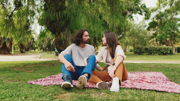 istock Happy smiling couple talking while sitting on blanket in park 1456352268