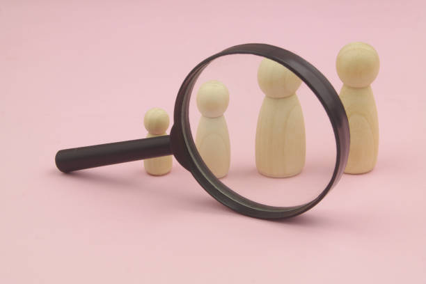 Different size female people figures under magnifying glass on pink background. stock photo