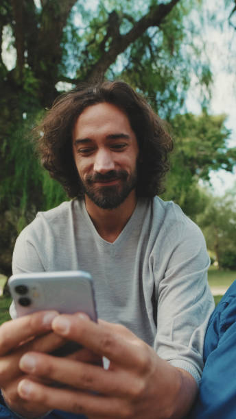 istock Young man using mobile phone while sitting on the lawn in the park 1456352775