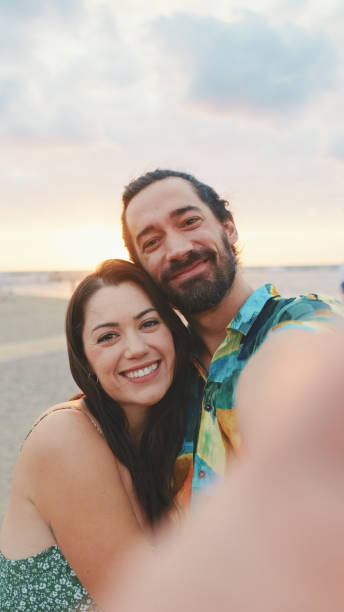 istock Laughing couple making video call while standing on the beach 1456352854