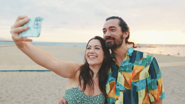 istock Laughing couple taking selfie on mobile phone while standing on the beach 1456352877