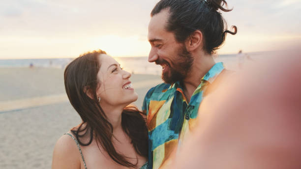istock Laughing couple making video call while standing on the beach 1456352935