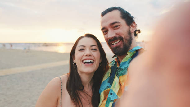 istock Laughing couple making video call while standing on the beach 1456352943