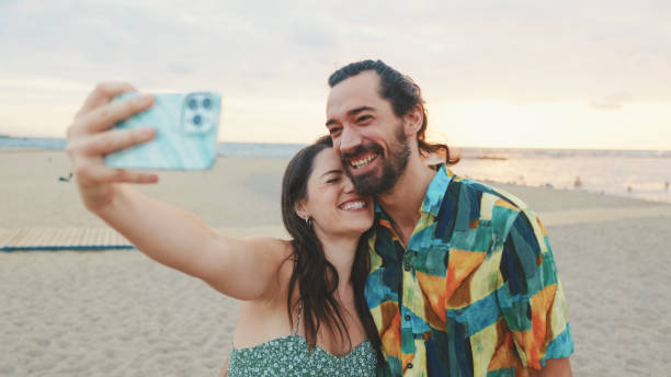istock Laughing couple taking selfie on mobile phone while standing on the beach 1456352964