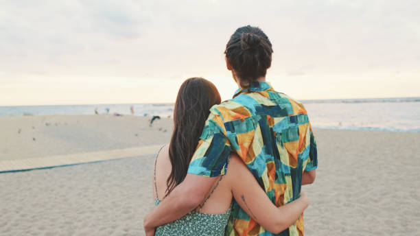 istock Young couple holding hands while standing on the beach. Back view 1456352990