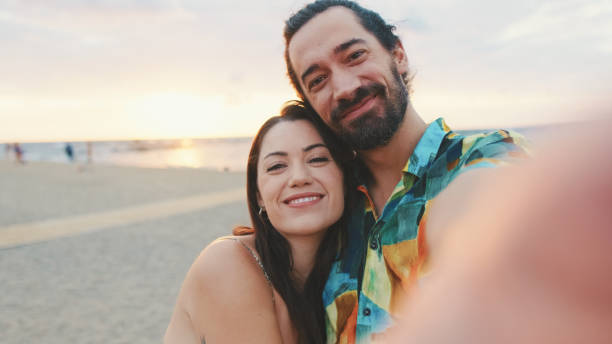istock Laughing couple making video call while standing on the beach 1456353023