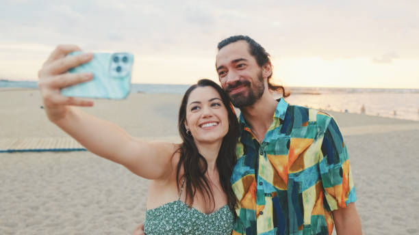 istock Laughing couple taking selfie on mobile phone while standing on the beach 1456353031