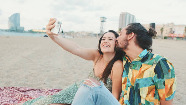 istock Happy couple taking selfie on mobile phone while sitting on the beach 1456353038