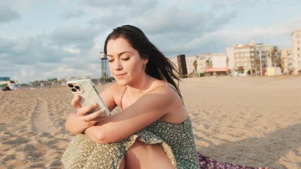 istock Young woman sitting on sandy beach and using mobile phone 1456353043