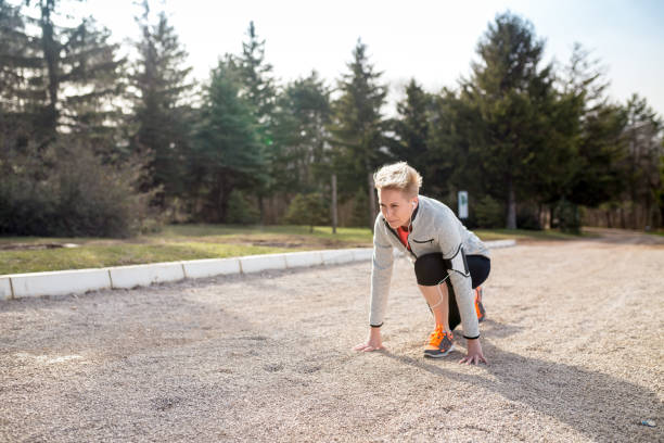 Ready to go! Female athlete on the starting line of a stadium track, preparing for a run. Sunny spring day, young sport lady is in a fashionable outfit, sneakers